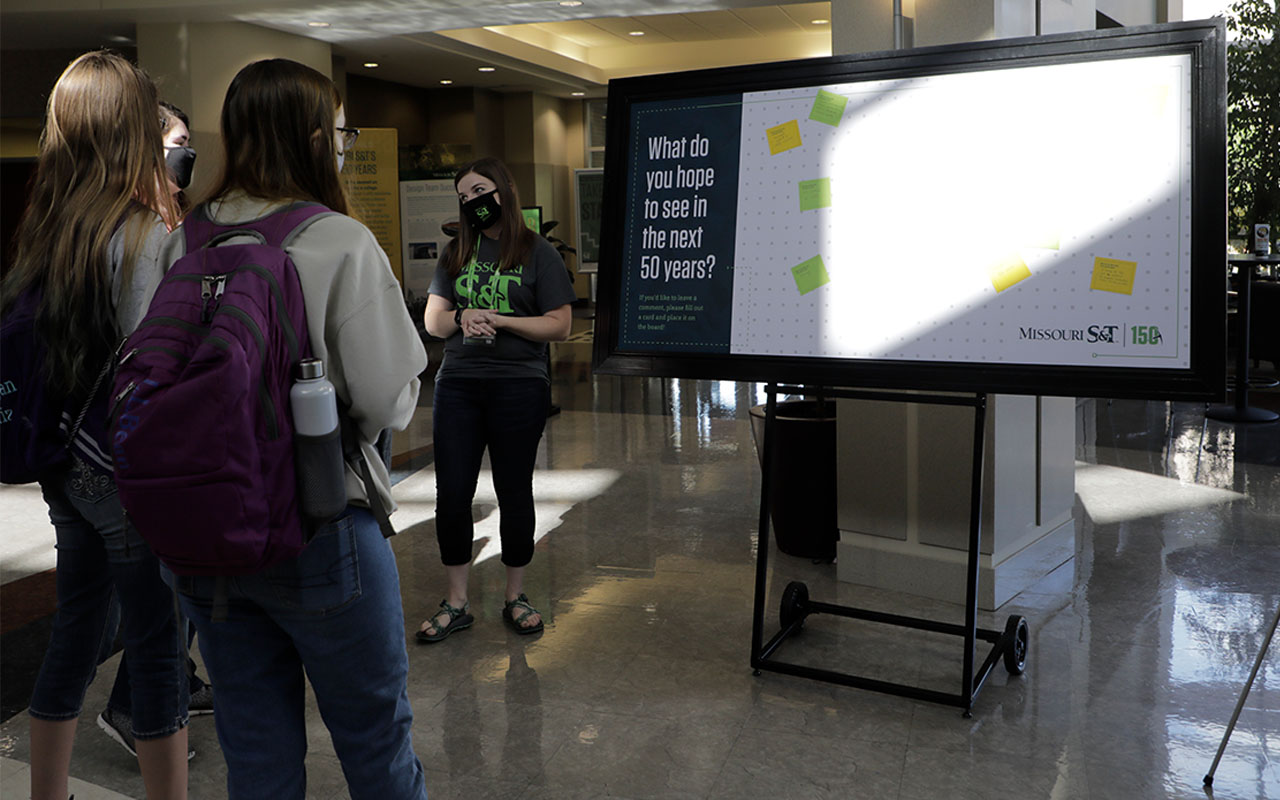 Students look at board with post-its sharing ideas for the next 150 years